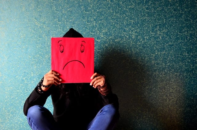 Person holding a red piece of paper with a frowny face on it