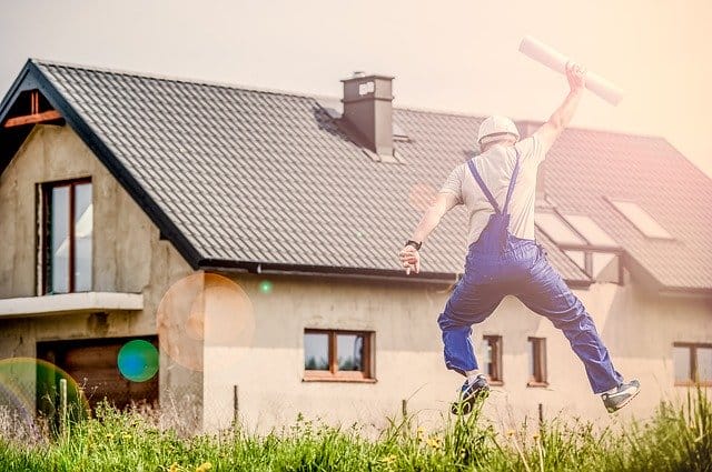 A construction worker jumping in front of a house